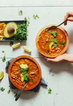 two bowls of soup with avocado and tortilla chips on the side