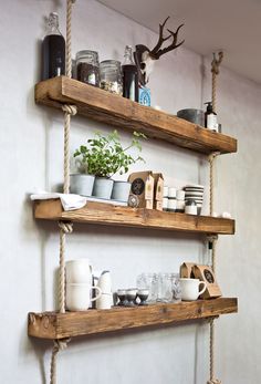 two wooden shelves with plants and cups on them, hanging from ropes in a kitchen