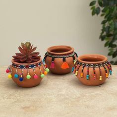 three clay pots with colorful beads and tassels sit on a table next to a potted plant