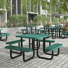 there are many green tables and benches on the sidewalk in front of some buildings with potted plants