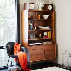 a living room with a bookcase, chair and table next to a large window