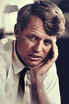 a man in a white shirt and tie is holding his hand to his face while looking at the camera