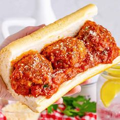 a hand holding a sandwich filled with meatballs and marinara sauce on top of bread