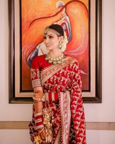 a woman in a red and gold sari standing next to a painting on the wall