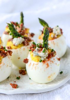 four deviled eggs on a white plate topped with green garnish