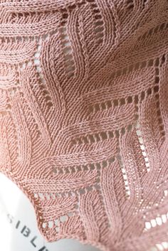 a pink knitted shawl hanging from a hook on a clothes hanger in front of a book