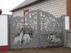 a metal gate with two dogs and trees on the front, in front of a brick building