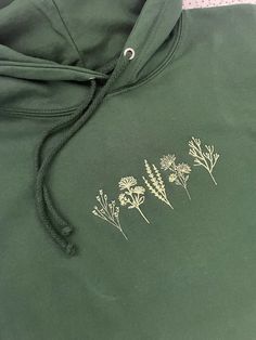 Super Comfortable lightweight Forest Green hoodie with embroidered Wildflowers design in light green.  Featuring the Boo and Beast heart logo embroidered on the back collar. Available in different sizes, if your colour option isn't listed, please get in touch as we might be able to assist. Material: 80% combed cotton / 20% polyester.  Double fabric hood with matching coloured cords. Fabric weight: 280gsm Forest Green Hoodie, Flower Hoodie, Cheer Shirts, Heart Logo, Green Hoodie, Simple Flowers, Colorful Hoodies, Hoodie Design, Logo Embroidered