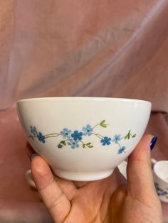 a hand holding a white bowl with blue flowers on it and two cups in the background