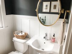 a white toilet sitting next to a bathroom sink under a round mirror in a bathroom