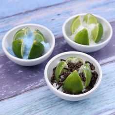 three small white bowls filled with fruit on top of a blue wooden table next to two limes