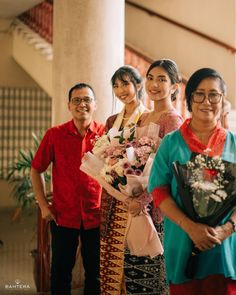 a group of people standing next to each other in front of a staircase holding flowers