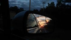 the rear view mirror of a car is shown as the sun sets in the distance