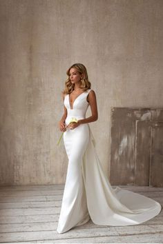 a woman in a white wedding dress standing on a wooden floor with her hands behind her back