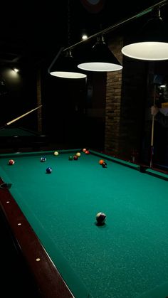 a pool table in a dark room with several lights hanging from it's ceiling