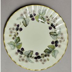 a white plate with blackberries and green leaves on the rim is sitting on a gray surface