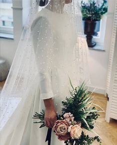 a woman in a wedding dress holding a bridal bouquet with flowers and greenery