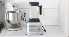 a silver blender sitting on top of a counter next to a metal bowl and mixer