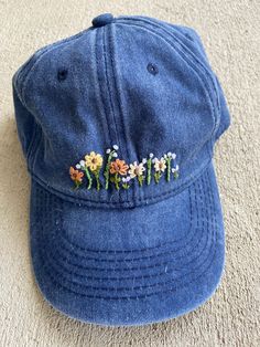 a blue hat with embroidered flowers on it sitting on the floor next to a carpet