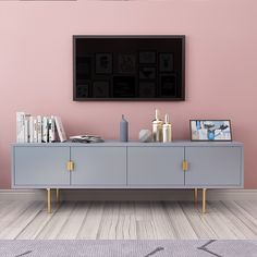 a tv is mounted on the wall above a gray cabinet with gold handles and two vases