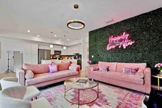 a living room filled with pink couches next to a wall covered in greenery