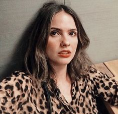 a woman with long hair wearing a leopard print shirt and looking at the camera while sitting on a bench