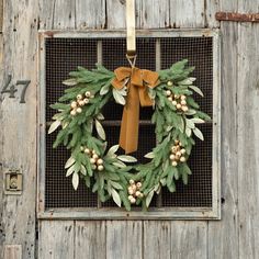 a wreath hanging on the side of a wooden door with a brown ribbon and bow