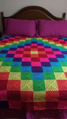 a multicolored blanket on top of a bed with purple sheets and pink pillows