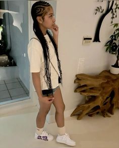 a girl with long hair and braids standing in front of a mirror wearing white sneakers