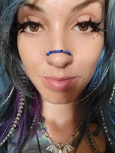 a close up of a person with blue hair and piercings on her nose, looking at the camera