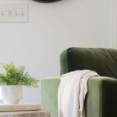 a green chair with a blanket on it next to a clock and plant in a white vase