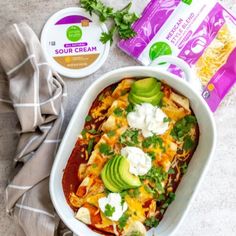 an enchilada casserole with sour cream and avocado on the side