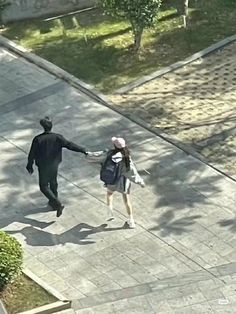 two people are walking down the street holding hands and one is wearing a backpack while the other holds his hand