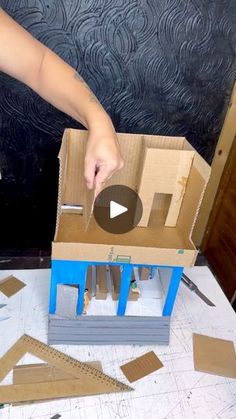 a person cutting out cardboard with scissors and tape on top of a box that is being made into a doll house