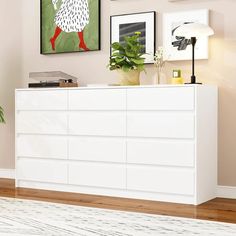 a white dresser sitting in a living room next to a painting and potted plant