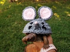 a hand holding a small turtle wearing a knitted mouse hat