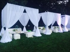 an outdoor wedding setup with white drapes and couches on the grass at night