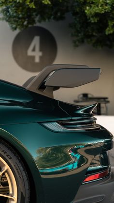 the rear end of a green sports car parked in front of a wall with numbers 4 on it