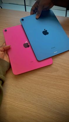 two ipads are sitting next to each other on a wooden table, one is pink and the other is blue