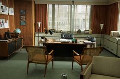 an office with two chairs and a desk in front of a large window that has curtains on it