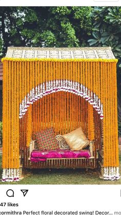 a bed made out of yellow and white sticks with pillows on the top, in front of some trees