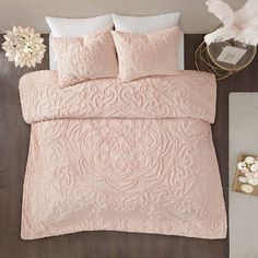 a bed with pink comforter and pillows on top of it next to a flower