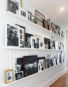 a wall filled with lots of pictures and framed photos next to a wooden floor in front of a white wall