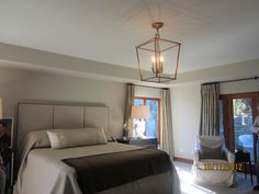 a bedroom with a bed, chair and chandelier hanging from the ceiling in front of two windows