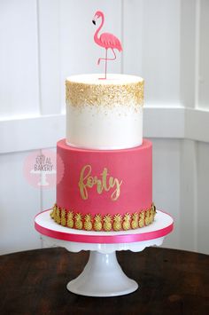 a pink and gold birthday cake with a flamingo topper sitting on a table