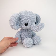 a hand holding a small blue crocheted stuffed elephant on a white table top