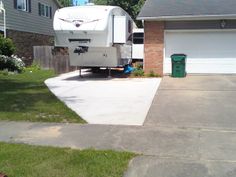 an rv parked in front of a house with two garages and a green trash can