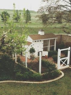 a small white house in the middle of a grassy area with trees and bushes around it