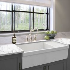 a white kitchen sink sitting under a window next to a bowl of fruit and vegetables