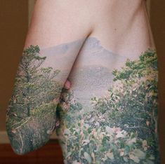 the back of a person's arm with trees and mountains on it